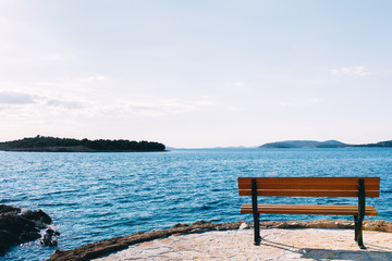 Fototapeta na wymiar Beautiful seascape and lonely bench. Bench on seaside of Adriatic coast in Primosten. Relaxing mood. Background with copy space. Romantic. Summer tourism. Travel concept. Bilo, Croatia