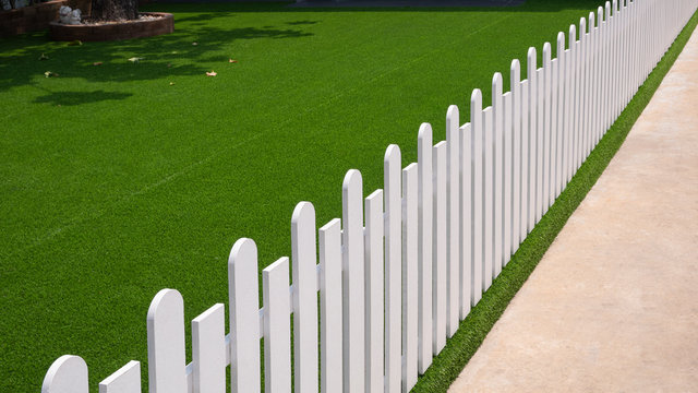 High angle and diagonal view of white artificial wooden fence on green artificial turf in front yard of home,  exterior architecture concept