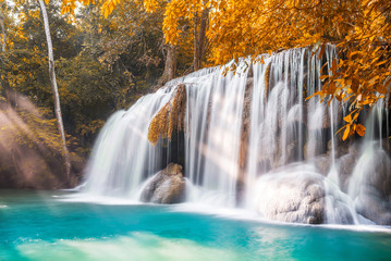 Waterfall and blue emerald water in autumn forest with sun flare and sunlight in morning. Erawan Waterfall step 2nd. Beautiful nature rock waterfall steps in rainforest at Kanchanaburi, Thailand