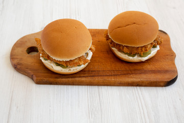 Homemade Burgers with fried chicken strips on a rustic wooden board on a white wooden background, high angle view.