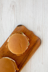 Homemade Burgers with fried chicken strips on a rustic wooden board on a white wooden table, top view. Flat lay, overhead, from above. Copy space.