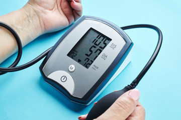 measuring blood pressure with electronic medical device over blue background.