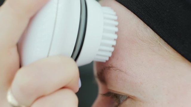 Young woman cleaning face using cosmetic face brush. Facial. Cosmetic procedures. At home. Close up