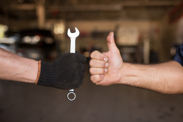 Close-up Thumb Up and Mechanics Hand with Tool. Automobile Master Wearing Gloves Showing Positive...