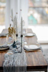 Wedding or festive table setting. Plates, wine glasses and cutlery with gray and bright blue decorative textile on wooden table. Beautiful arrangement.