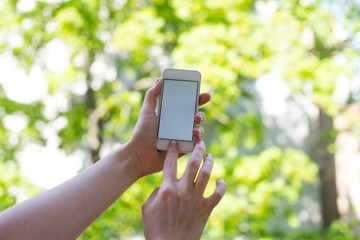 Mockup smartphone with empty screen in a green bokeh background. Young woman hand with phone on spring background. Smartphone in a woman hand on modern background.
