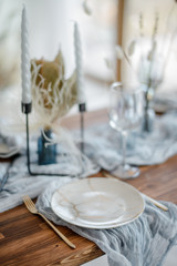 Closeup of dinner wooden table in dusty blue color. White plate with vintage golden fork and knife, candles on candlesticks, gauze napkins. Wedding dinner. Decor.