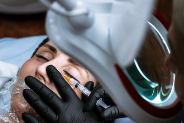 Beautician makes an injection of beauty. The doctor injects Botox into the area under the eyes of a young woman. Cosmetologist services