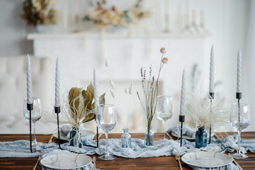 Autumn table decoration, wooden table served with dried flower, white plate, vintage cutlery, candeles with bright blue gauze tablecloth. Top view, selective focus.