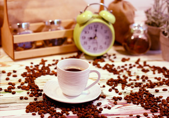 A cup of coffee on a platter with lots of sprinkled coffee beans. Alarm clock arrows at 9 am. Wooden textured table. Shy pastel background. Time to wake up in the morning. Natural food concept