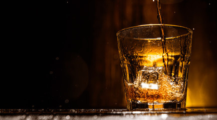 whiskey is poured into a glass with ice on a dark wooden background