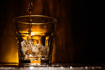 whiskey is poured into a glass with ice on a dark wooden background
