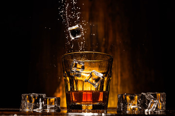 ice falls into a glass with expensive whiskey and spray flies in different directions