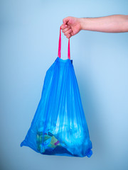 Men's hands holding used blue plastic garbage bag isolated on a blue background