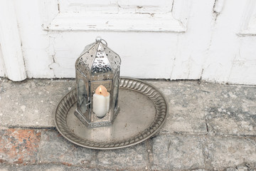 Ornamental Moroccan lantern on silver tray standing on stone ground. Old shabby door in background. Greeting card, invitation for Muslim holy month Ramadan Kareem. Festive still life, top view