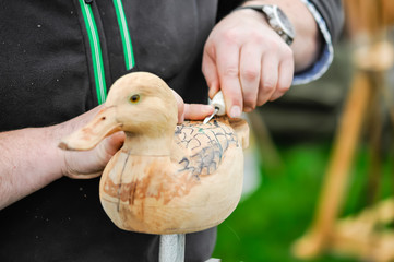 A man uses a small chisel to carve a wooden duck
