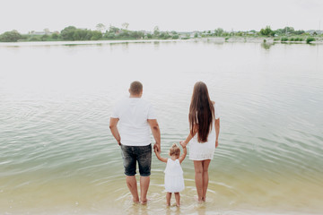 Fototapeta na wymiar beautiful and happy young family mom dad and daughter walking near the lake. summer holiday, family look.