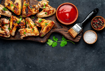 Grilled chicken wings in barbecue sauce on a wooden board on a concrete table with copy space for your text. © александр таланцев