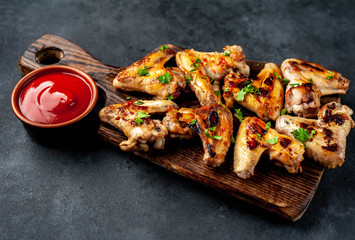 Grilled chicken wings in barbecue sauce on a wooden board on a concrete table.