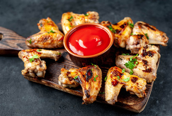 Grilled chicken wings in barbecue sauce on a wooden board on a concrete table.