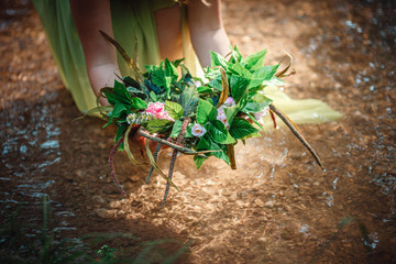 Beautiful young woman in a green dress and a wreath in a sunny forest
