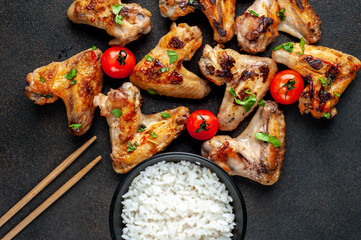 Grilled chicken wings in barbecue sauce and rice in a bowl on a concrete background