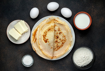 The recipe for making thin home-made pancakes. Ready-made thin pancakes, flour, eggs, butter, milk, sugar on a stone background