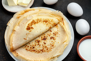 The recipe for making thin home-made pancakes. Ready-made thin pancakes, flour, eggs, butter, milk, sugar on a stone background