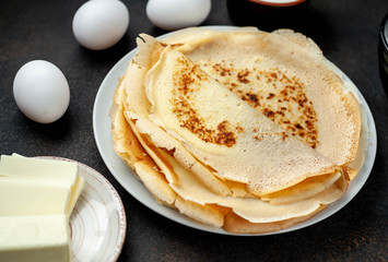 The recipe for making thin home-made pancakes. Ready-made thin pancakes, flour, eggs, butter, milk, sugar on a stone background