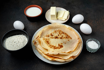 The recipe for making thin home-made pancakes. Ready-made thin pancakes, flour, eggs, butter, milk, sugar on a stone background