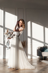 A beautiful bride in a white wedding dress is holding a bouquet of dried flowers in the interior of the Studio. Fashionable wedding style. Young bride.