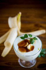 Homemade sweet yogurt with slices of ripe banana and caramel in a glass bowl
