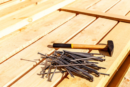 Iron nails and a hammer on a wooden background. Long, metal, carpenter's nails and a mallet lie on a bar for construction. Fixing tool. Side view. space for text.
