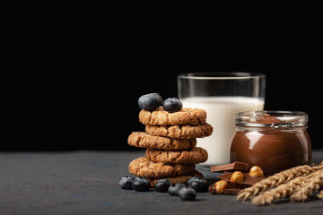 Homemade oatmeal cookies with a stuffing of blueberry and chocolate with hazelnut, chocolate paste and milk on background. Still life