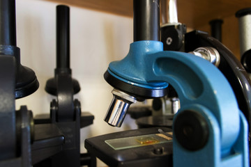 Close up blue and black microscopes stand on cabinet shelf. Laboratory equipment kit. Science and biology concept.