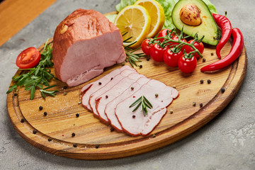 Sliced ham with spices, lettuce, avocado and tomatoes on wooden cutting board. Сold meat plate. Fresh prosciutto
