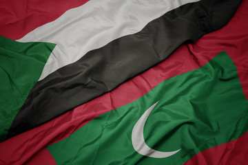waving colorful flag of maldives and national flag of sudan.