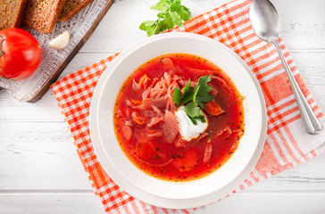 white plate of borscht with sour cream and herbs, a spoon on a checked towel, Ukrainian red soup with beetroot