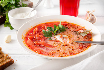 Ukrainian red borscht with parsley and sour cream, a spoon, pieces of bread ,a glass of juice on a white wooden background