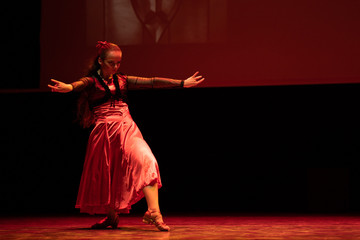 Dancer in a red dress dancing Spanish flamenco on the stage in the theater