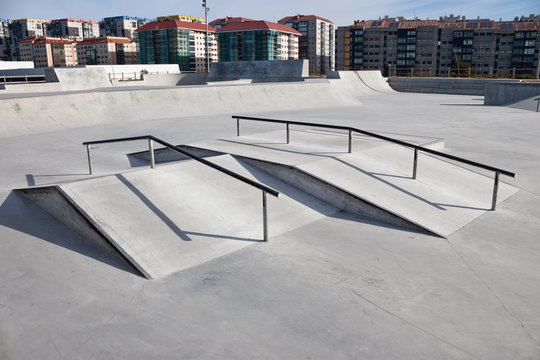 Sloped metal rails for grind tricks in an empty concrete skatepark