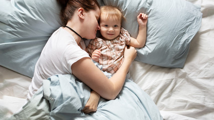 Mom in pajamas with baby sleeping on bed, top view