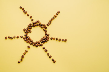 Coffee beans on a yellow background in the form of the sun. Caffeine morning drink. Closeup of bean grains.