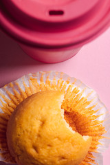 Bitten muffin and a pink cup of coffee above view.