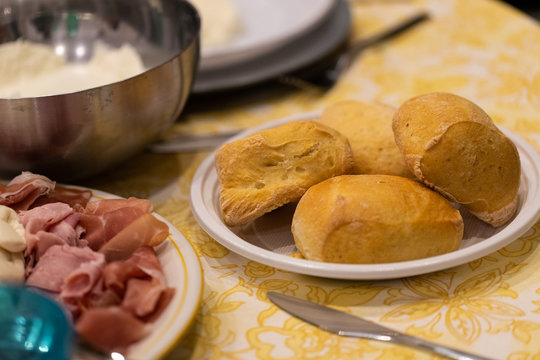 A dinner at home with the family. A table set with small loafs served on a plastic plate and a plate with ham.