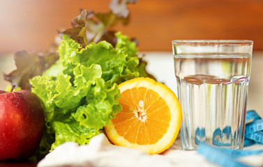 salade leaf. orange, cup of water and measuring blue tape on brown background , healthy lifestyle and drinking water concept
