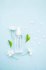 Hand antiseptic in spray bottle and beatiful blooming cherry tree flowers and fresh green leaves on blue background. Stop coronavirus concept.