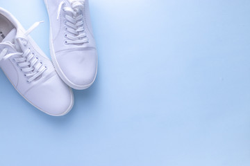 White sneakers on light blue colour background, flat lay top view minimal background. 
