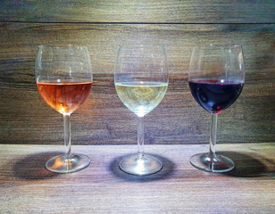 Three glasses of wine on a wooden texture background. rose wine, white wine, red wine