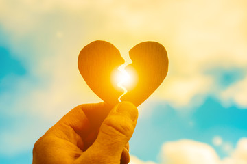Broken heart in a man’s hand on a sunset background. Parting, stop loving, break your heart....